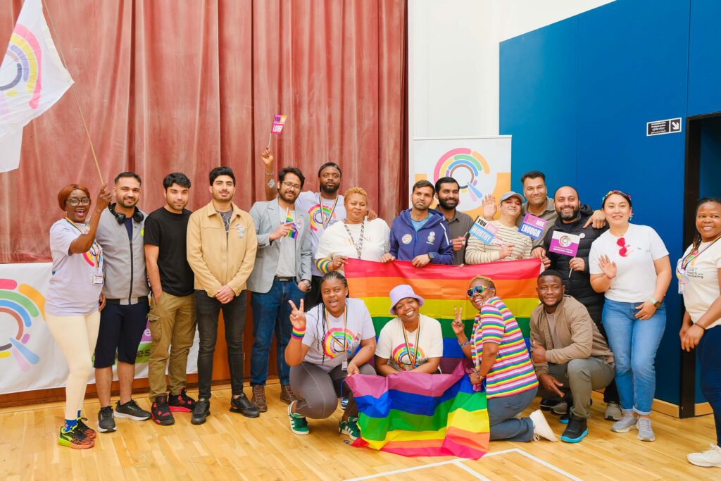 A group of LGBT New Scots at our Pride Breakfast event, holding Pride flags under a LGBT Health and Wellbeing banner
