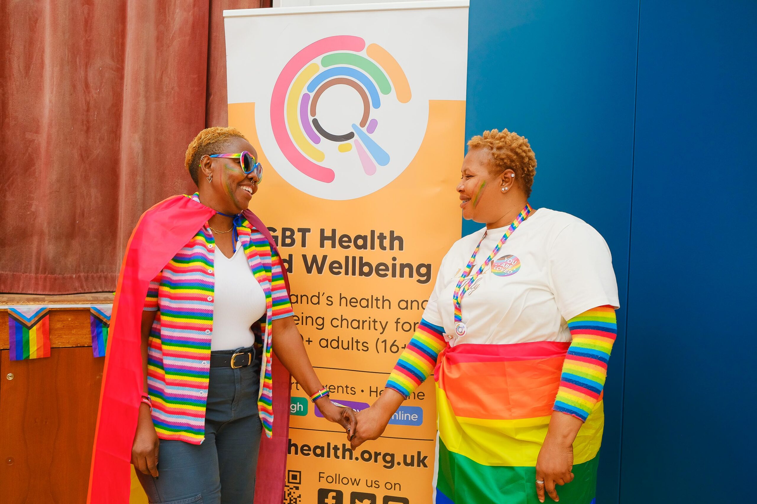 Two New Scots holding hands under an LGBT Health and Wellbeing banner