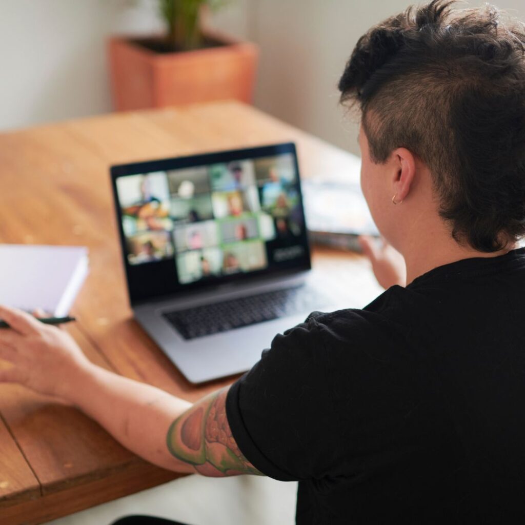 A person is seated at a table, working intently on their laptop.
