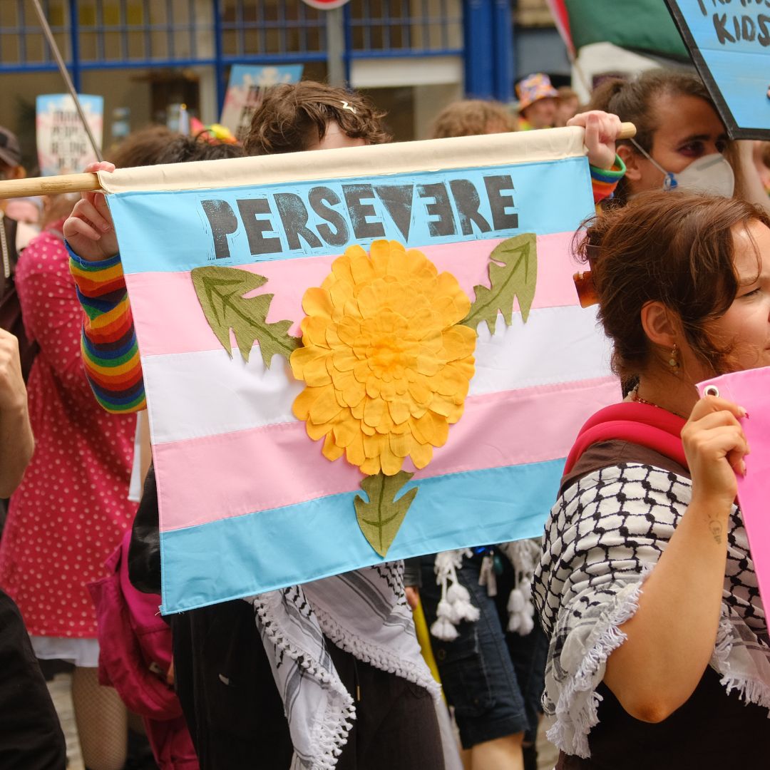 Community members at Pride Edinburgh holding a trans flag with text 'Persevere'