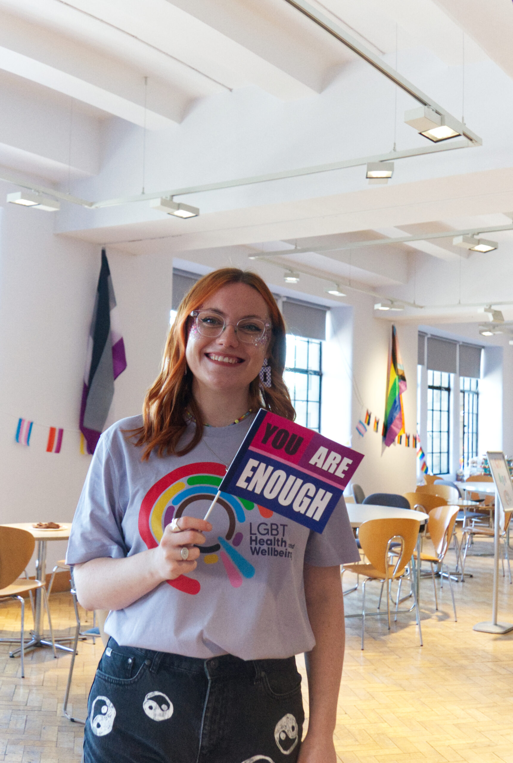 A photo of Rebecca smiling waving a bisexual flag with text 'You are enough'