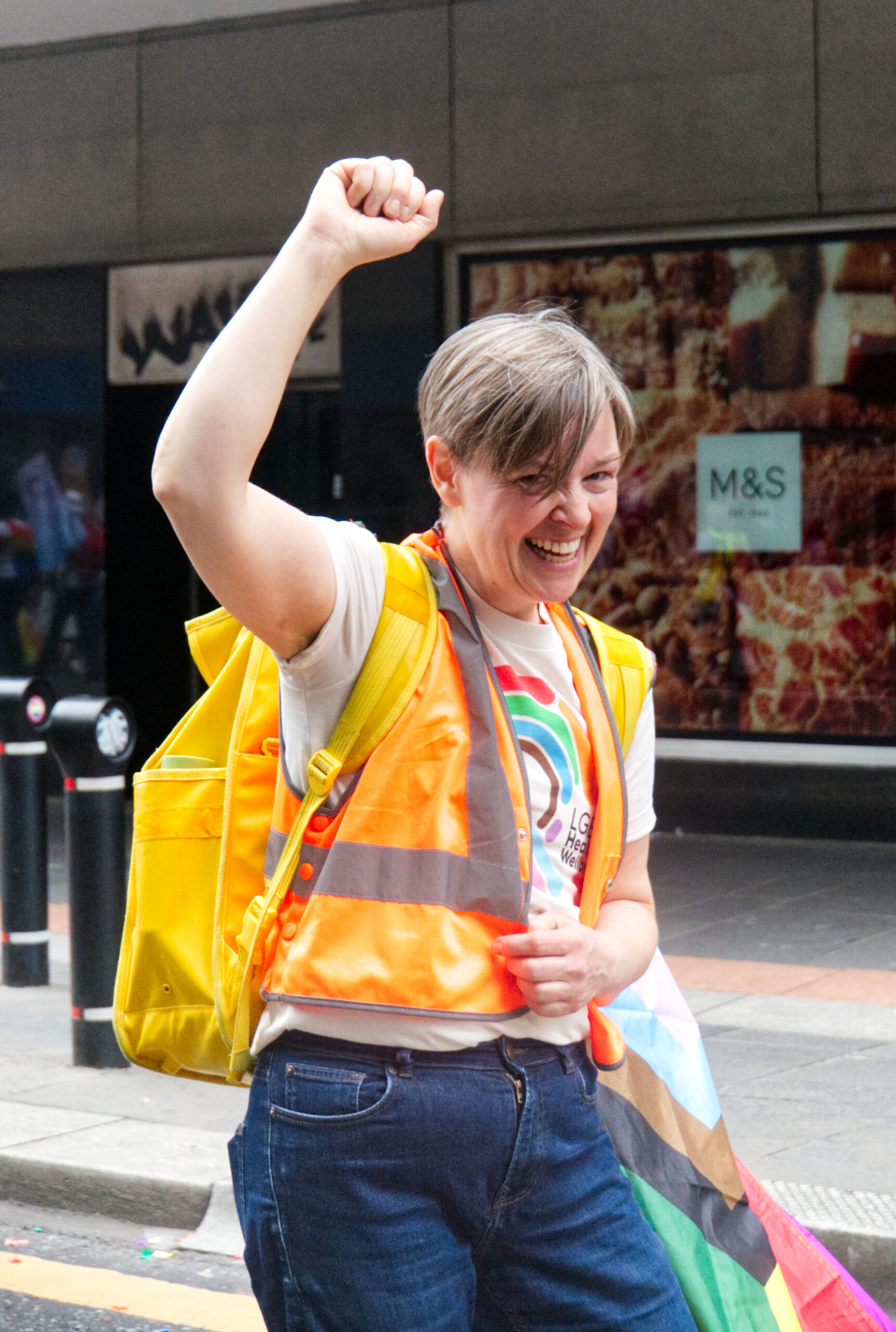 A staff member of LGBT Health and Wellbeing at a Pride March smiling with their fist in the air