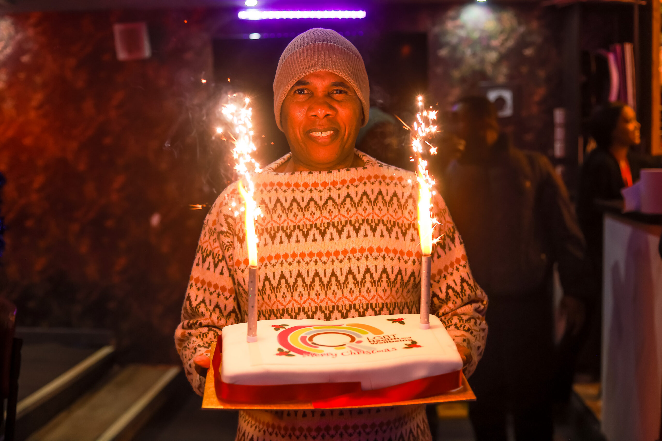 A LGBT Health and Wellbeing volunteer holding a birthday cake with our logo on it
