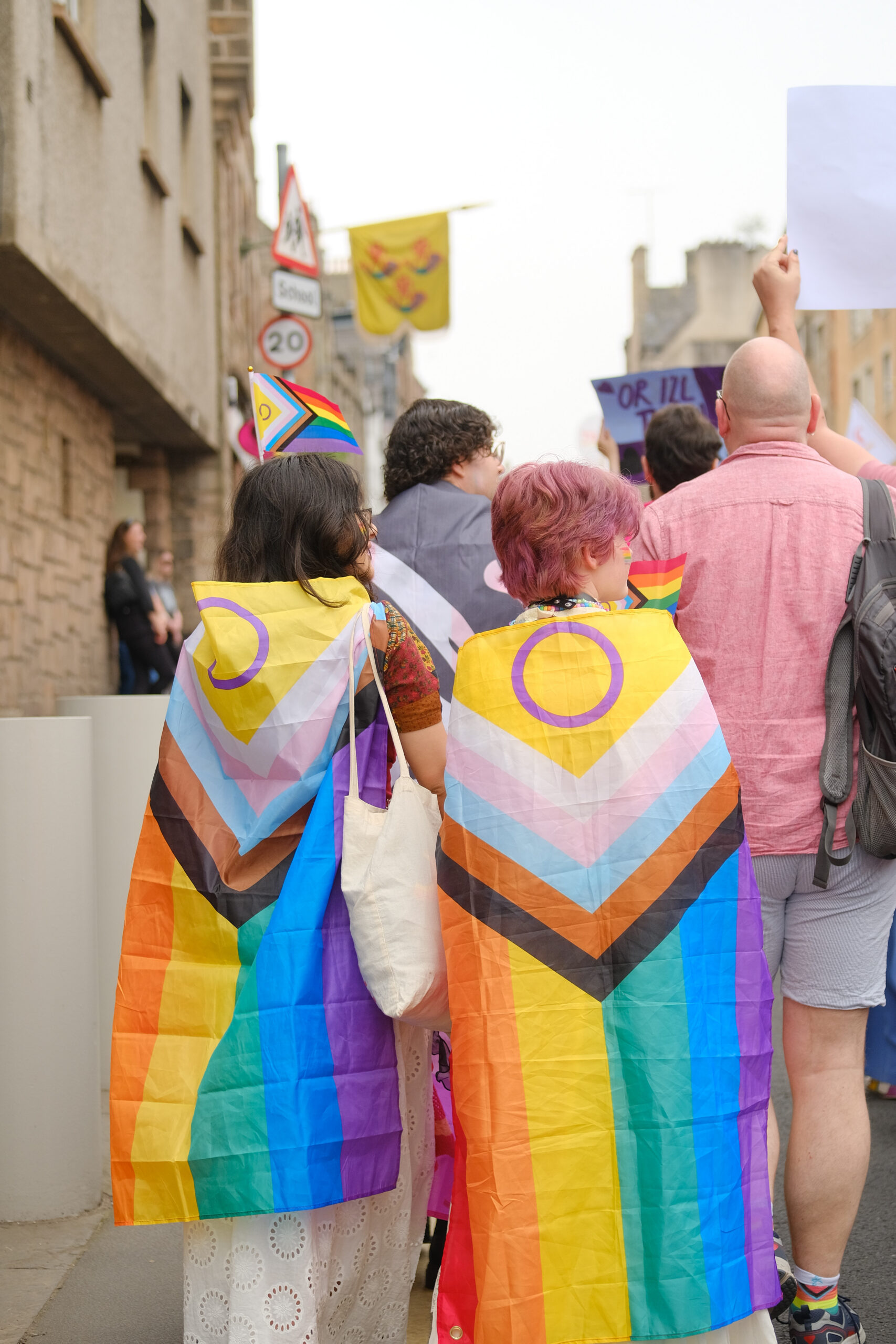 Two community members wearing progress Pride flag, marching at Pride Edinburgh