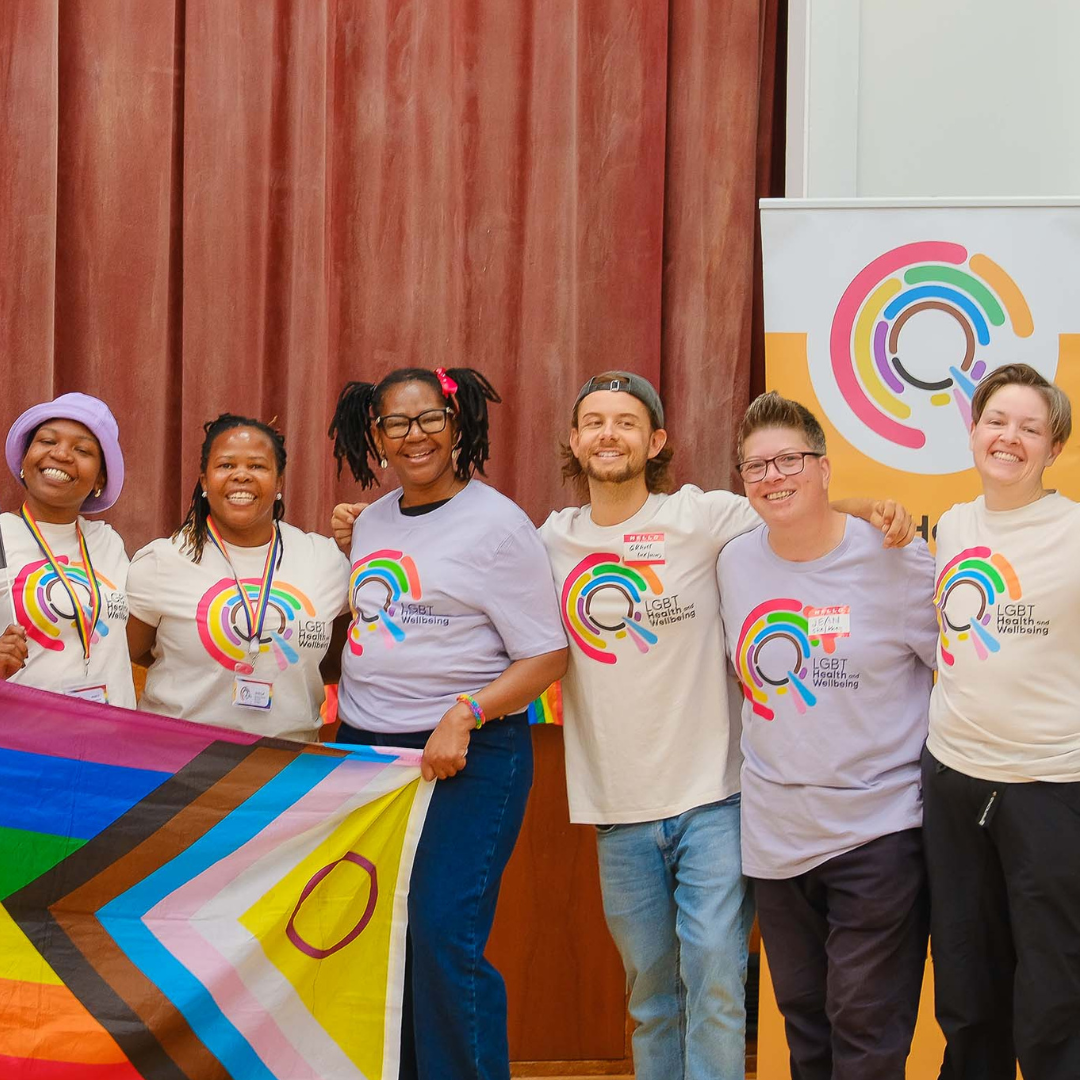 A group of LGBT Health and Wellbeing staff and volunteers holding a progress Pride flag